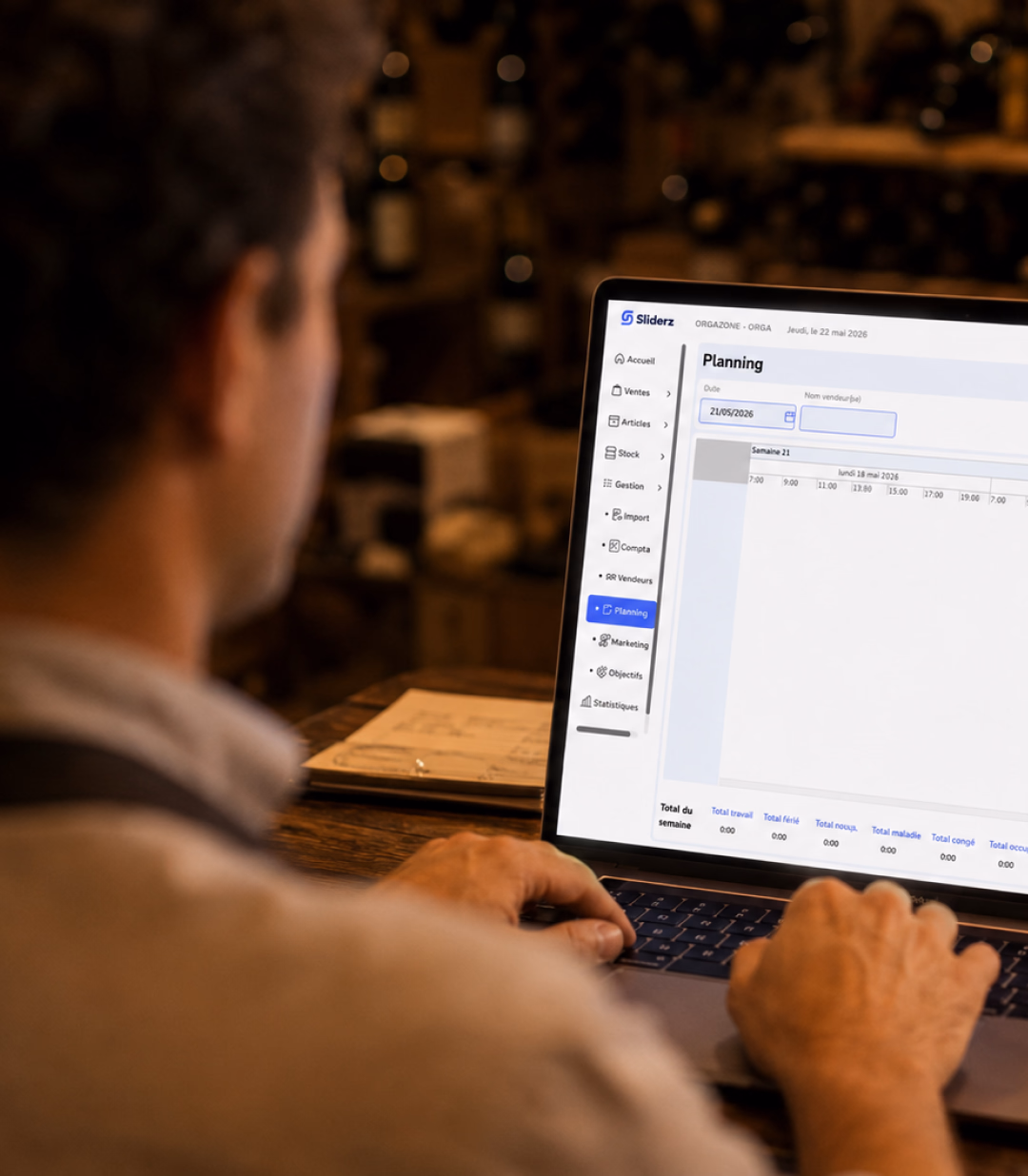 Caviste consultant le planning Sliderz sur ordinateur portable dans sa cave à vin